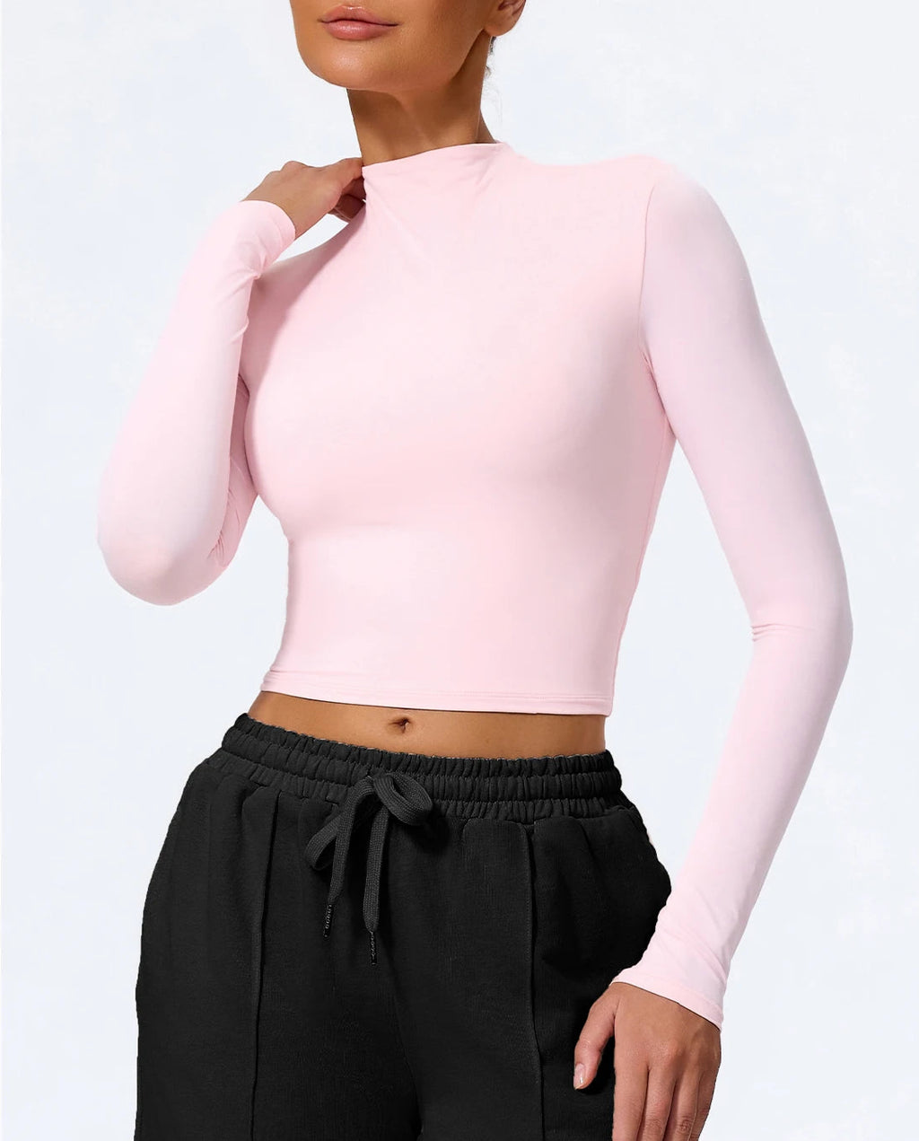 Person wearing a pink long-sleeve top and black pants on a white background