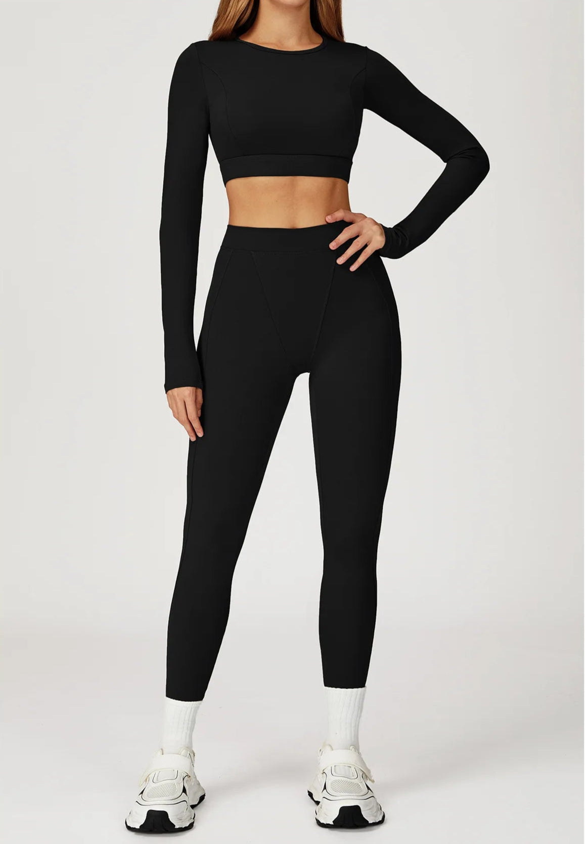 Person wearing a black long-sleeve crop top and leggings on a white background