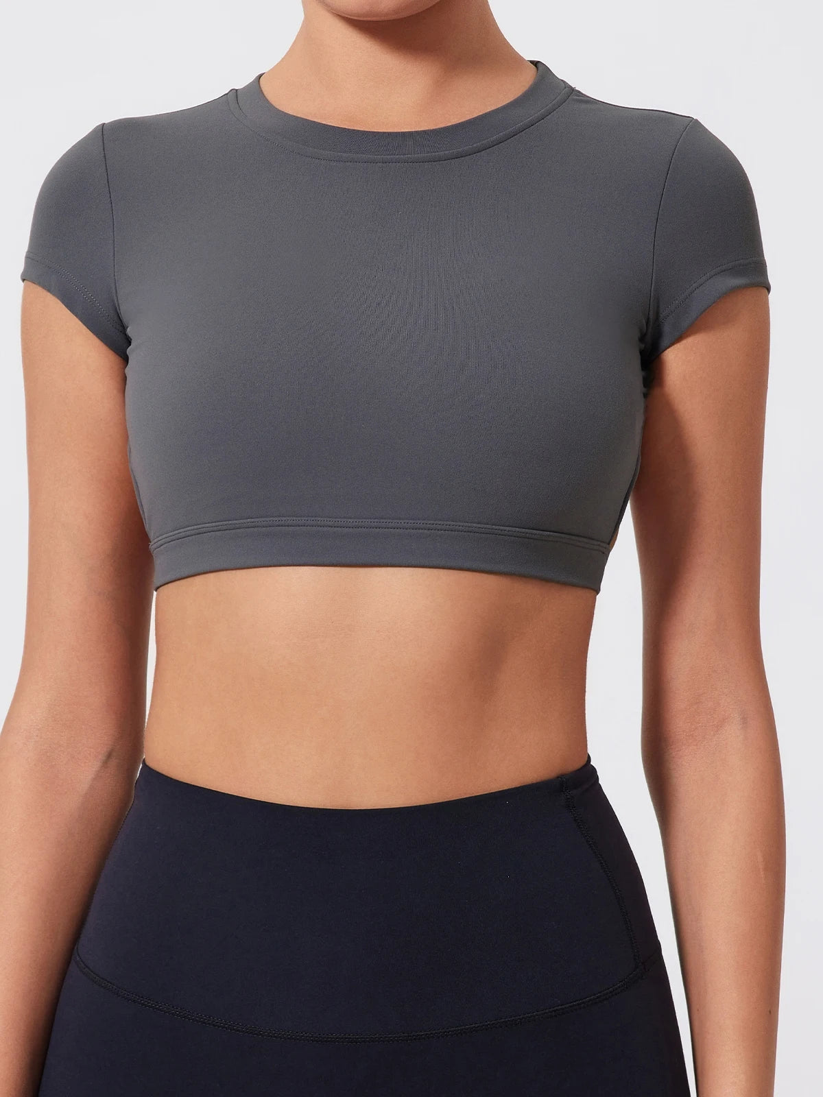 Person wearing a gray crop top and black leggings on a light gray background