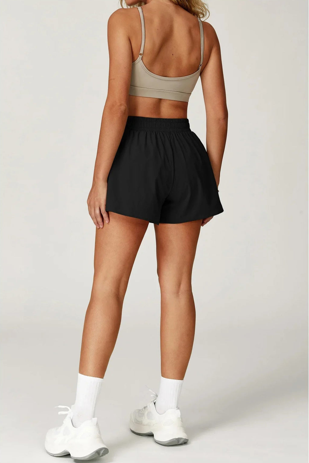 Person wearing a sports bra and black shorts on a plain background